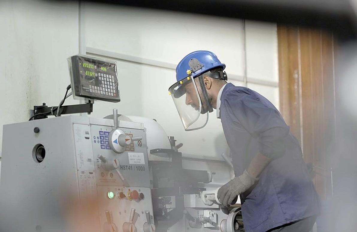 A technician in a face shield operating a lathe