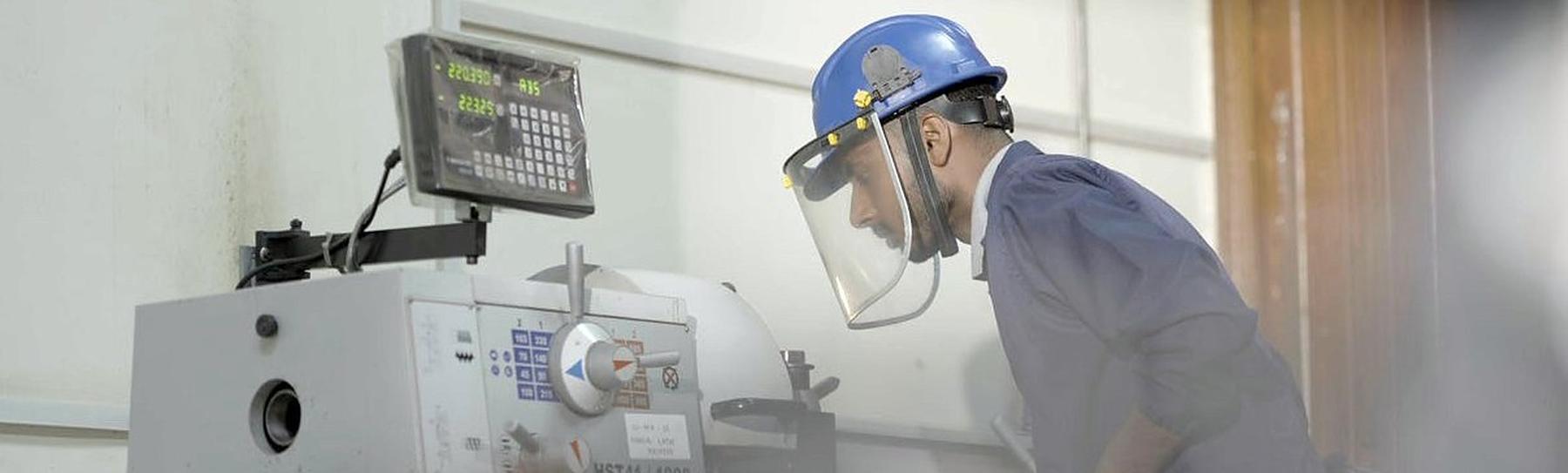 A technician in a face shield operating a lathe in a workshop