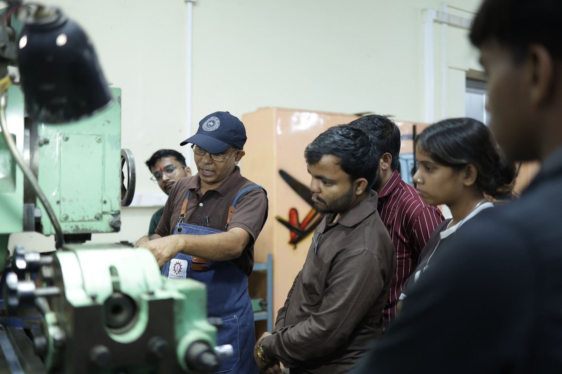 A faculty member guiding students on a lathe in a workshop